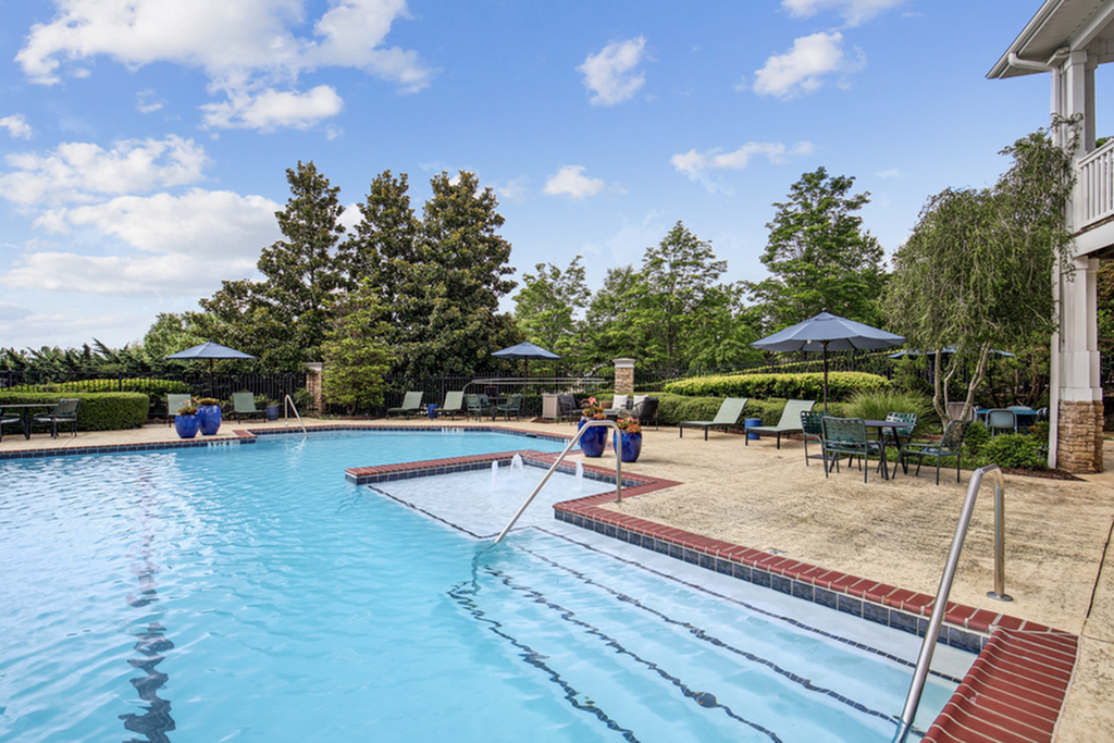 Inviting outdoor pool area with elegant lounge chairs, umbrellas, and lush greenery, perfect for a relaxing day under the sun.