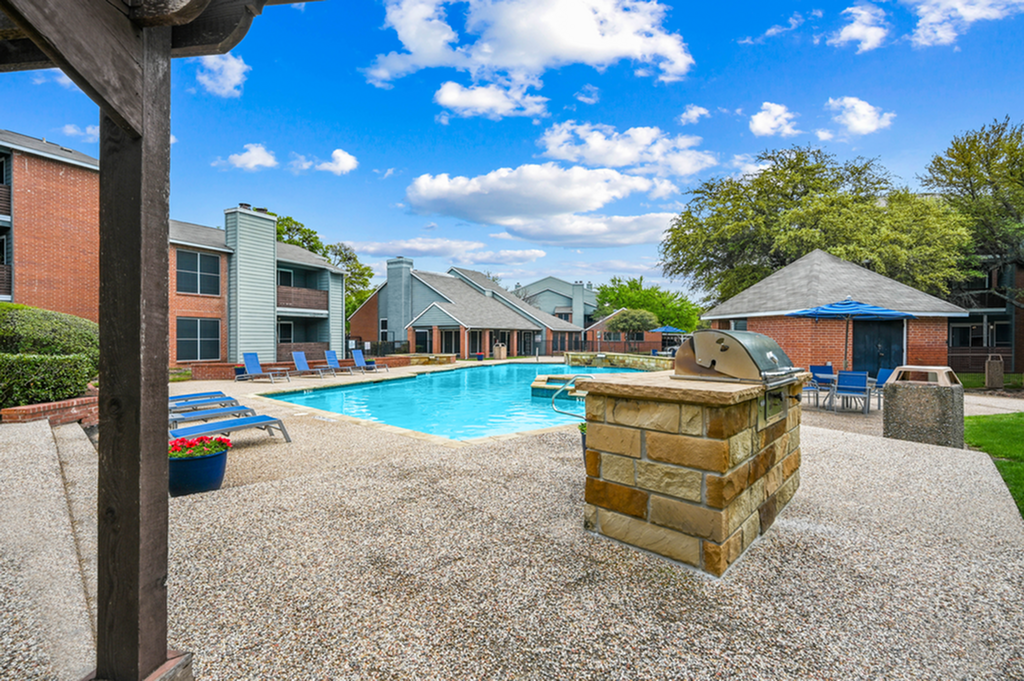 Charming apartment community featuring a pristine swimming pool, stylish lounge chairs, and a modern grill area under a bright blue sky.