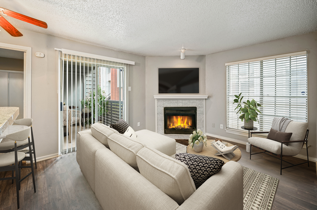 Inviting living room with a cozy fireplace, modern sofa, and natural light from large windows, opening to a lush patio area.