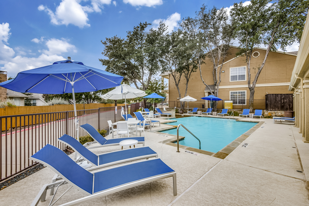 Inviting swimming pool area with vibrant blue loungers and umbrellas, surrounded by lush trees, perfect for relaxation and enjoyment.
