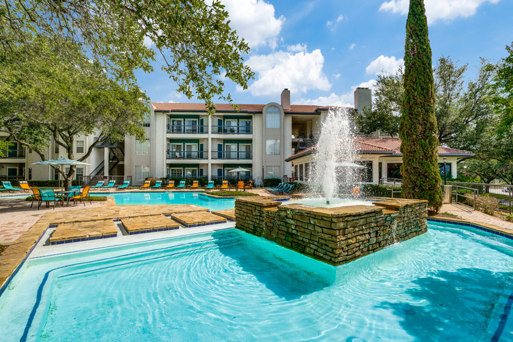 Charming apartment community with a sparkling pool, elegant central fountain, and lush green surroundings.