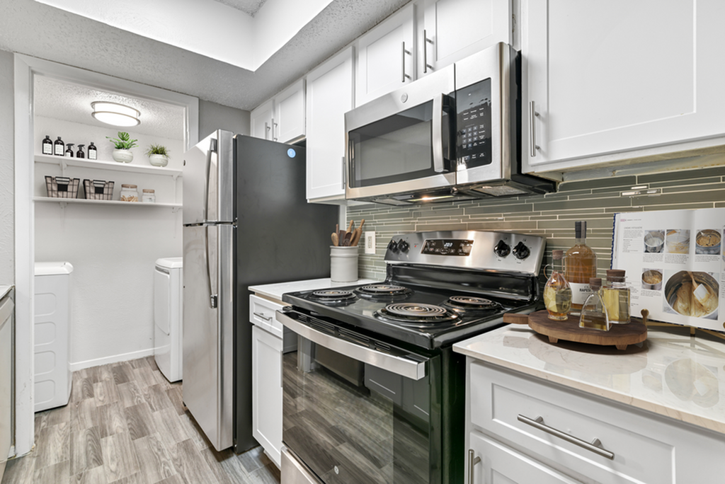 Modern kitchen with sleek stainless steel appliances, elegant white cabinetry, and stylish open shelving, featuring a convenient laundry area.