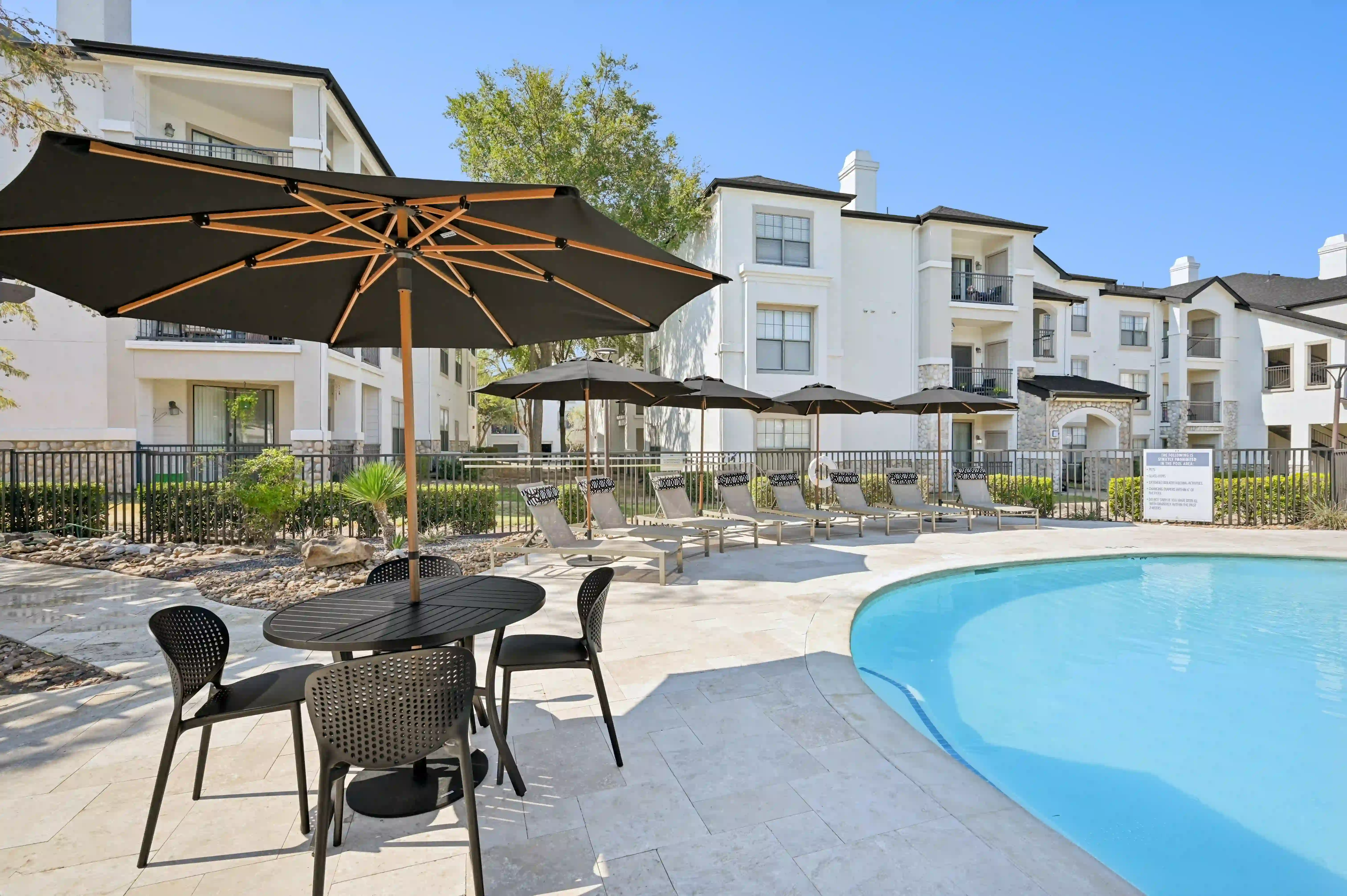 Resort-style swimming pool with lounge chairs, shaded patio seating, and surrounding apartment homes.