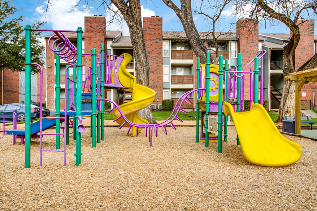 Vibrant playground area with colorful slides and climbing structures set against a backdrop of charming brick apartments.