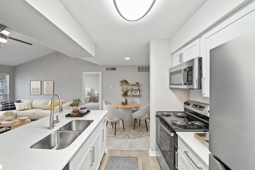 Modern open-concept kitchen and living area, featuring sleek stainless steel appliances and elegant white cabinetry, with a cozy dining nook in a bright and inviting space.
