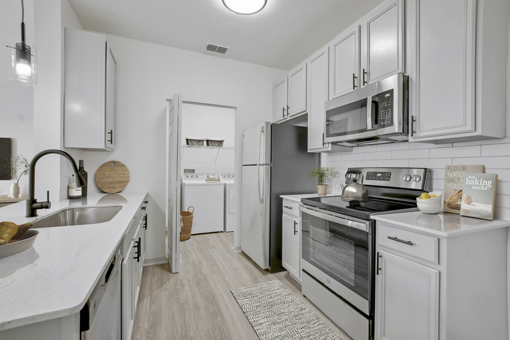 Sleek modern kitchen with elegant white cabinetry and stainless steel appliances, featuring a cozy laundry area in the background.