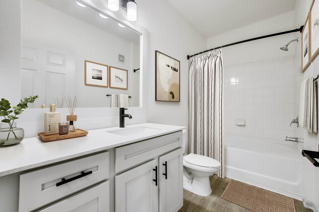 Modern and elegant bathroom with sleek white vanity, stylish large mirror, and a cozy bathtub, creating a serene and inviting atmosphere.