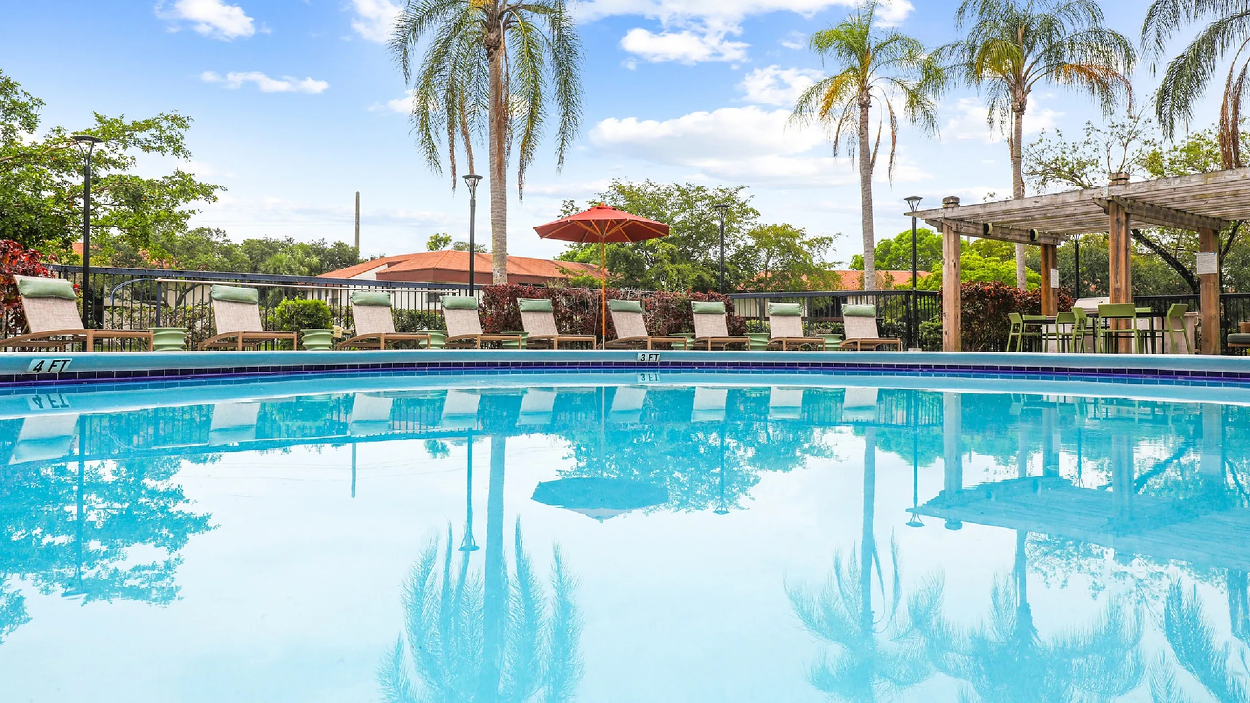 Outdoor swimming pool, surrounded by lounge chairs, palm trees, and a red umbrella