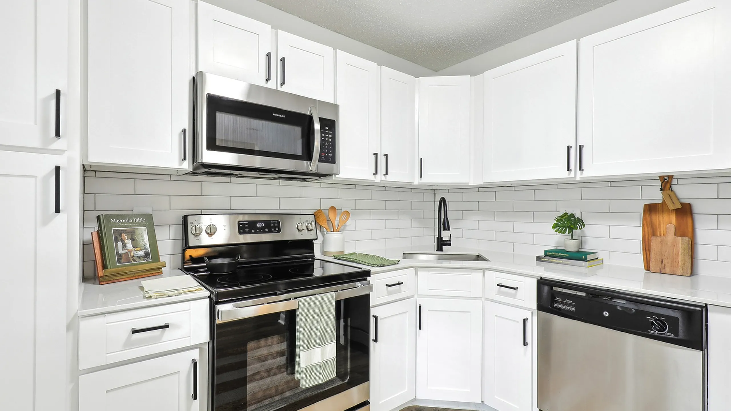 Modern white kitchen with stainless steel appliances, subway tile backsplash, and black hardware. Clean and minimalist design.
