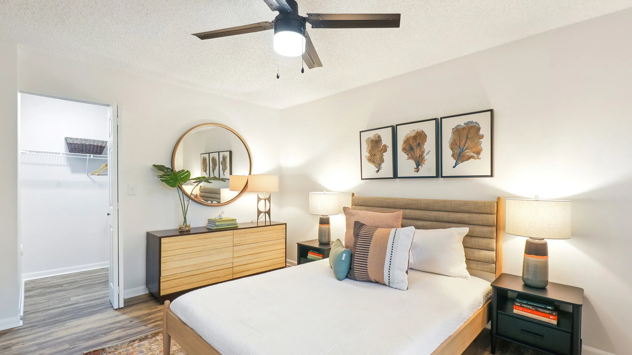 Bedroom with king sized bed and headboard with pillows, dresser, circular mirror, and ceiling fan light fixture