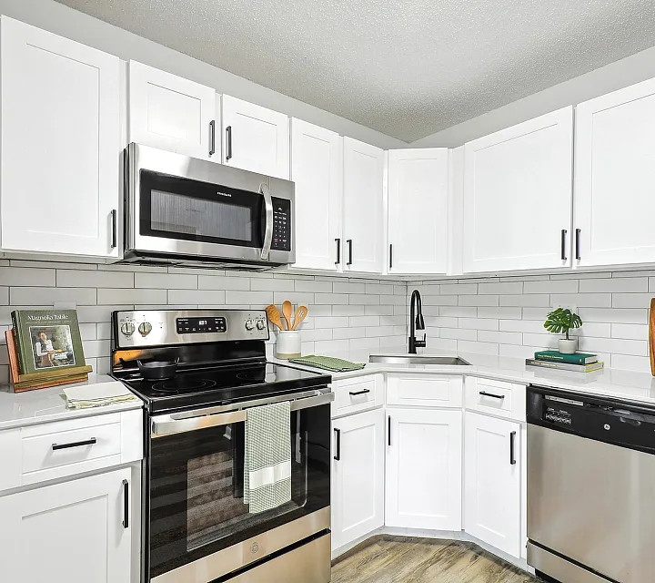 Staged renovated kitchen with white shaker cabinets, white quartz counter tops, white subway backsplash, stainless steel appliances, and hardwood-style flooring.
