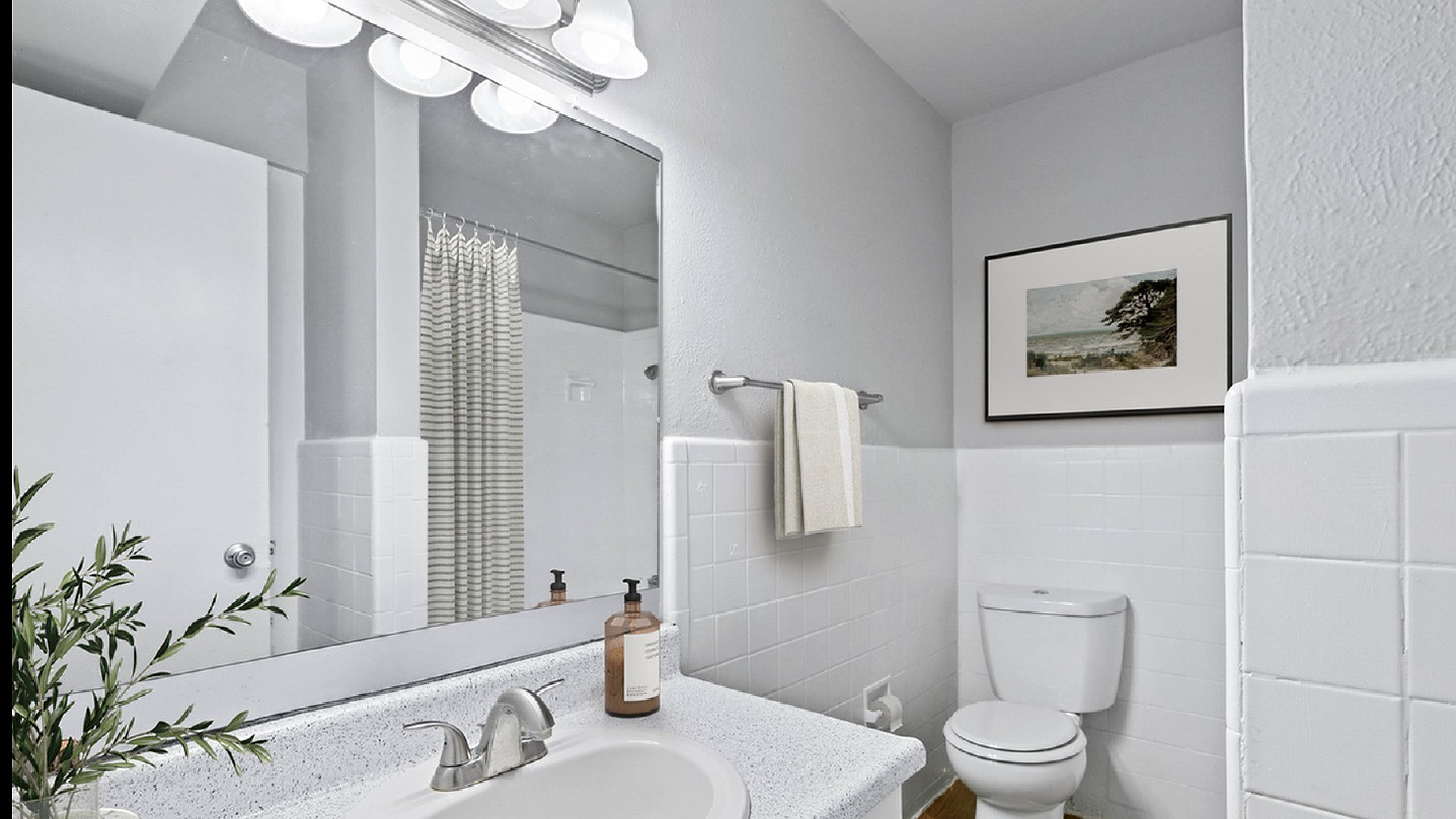 Bathroom with quartz counters, large mirror, vanity lighting, and white cabinetry