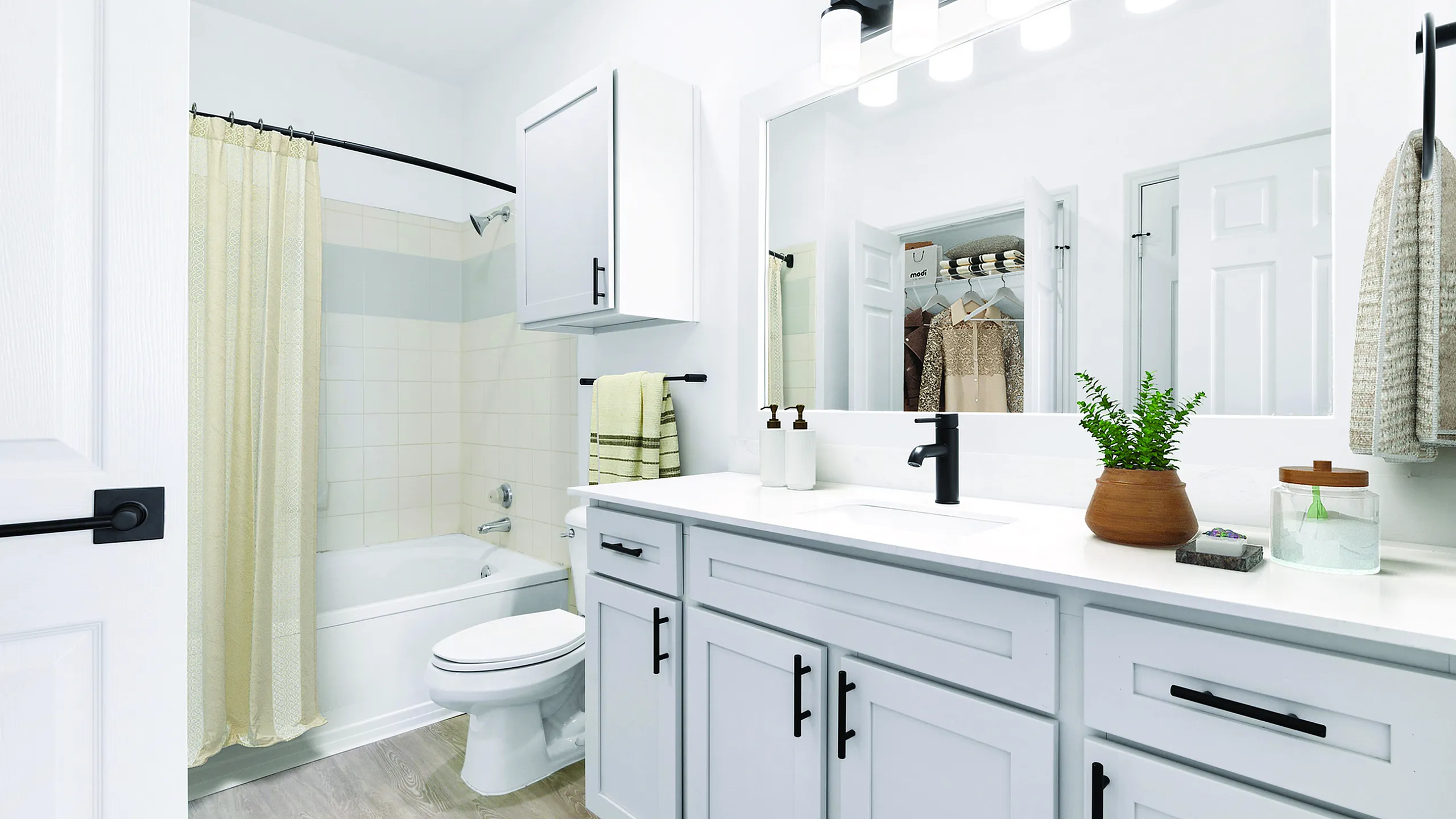 Bright and modern bathroom showcasing sleek white cabinetry, elegant fixtures, and a potted plant for a touch of green.