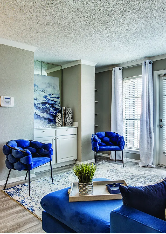 Chic living room with vibrant blue chairs and sofa, complemented by elegant decor and abundant natural light through large windows.