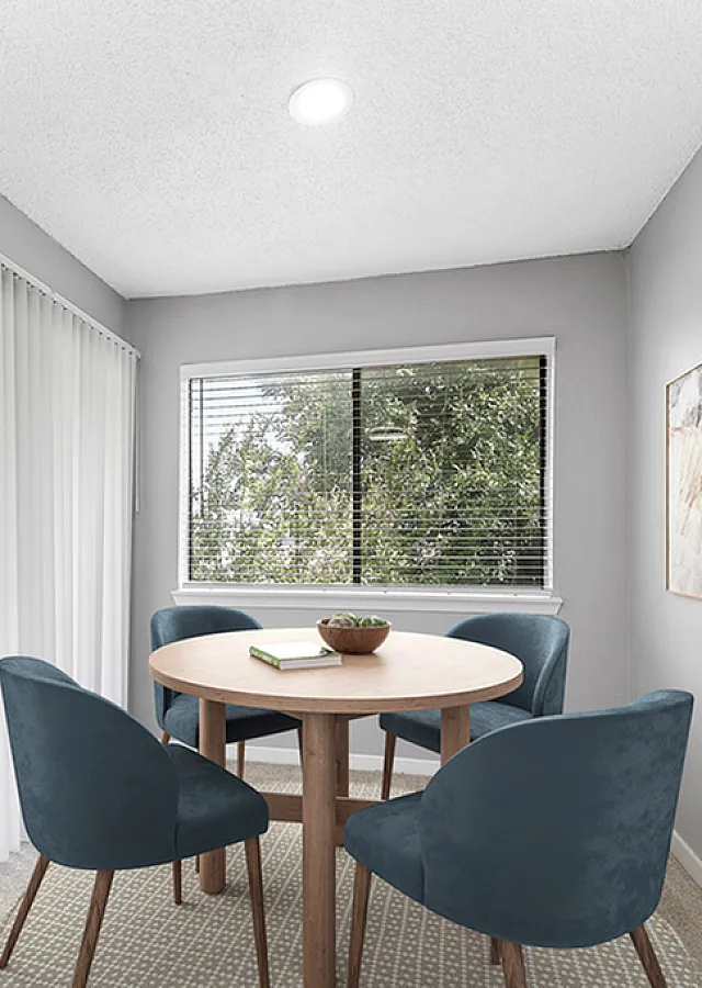 Bright dining area with a round wooden table, elegant blue chairs, large windows, and serene wall art creating an inviting space.