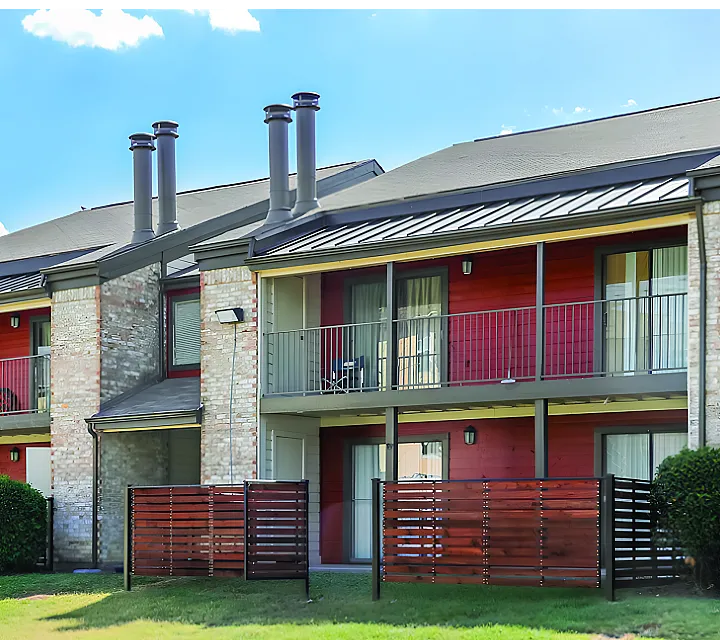 Charming apartment complex with modern balconies, vibrant red accents, and lush green surroundings under a bright blue sky.