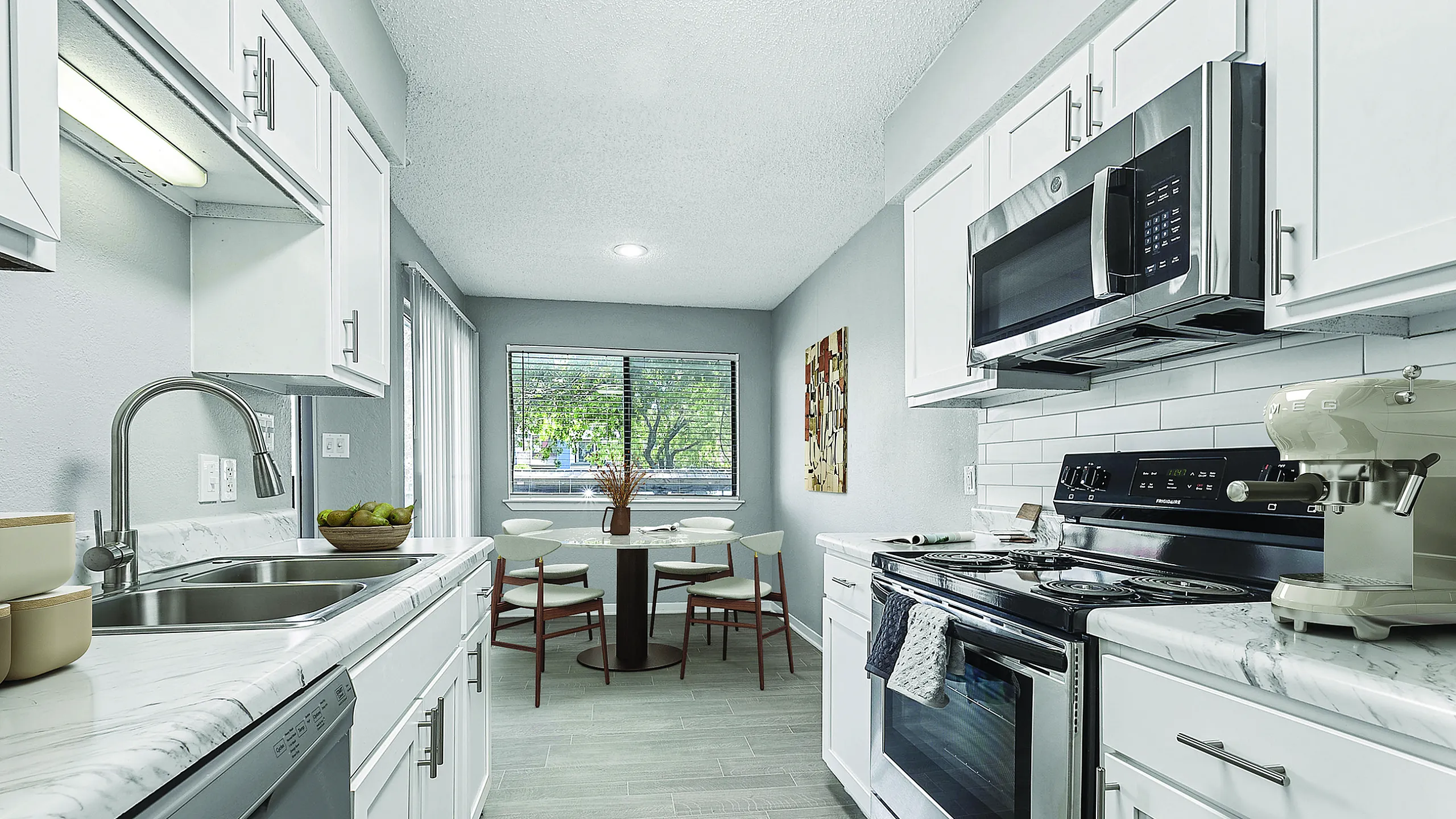 Modern kitchen with sleek white cabinetry, stainless steel appliances, and a cozy breakfast nook overlooking lush greenery.