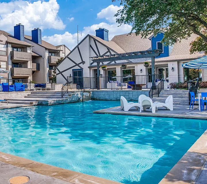 Charming residential complex featuring a sparkling pool with elegant loungers and vibrant blue umbrellas against a picturesque backdrop.