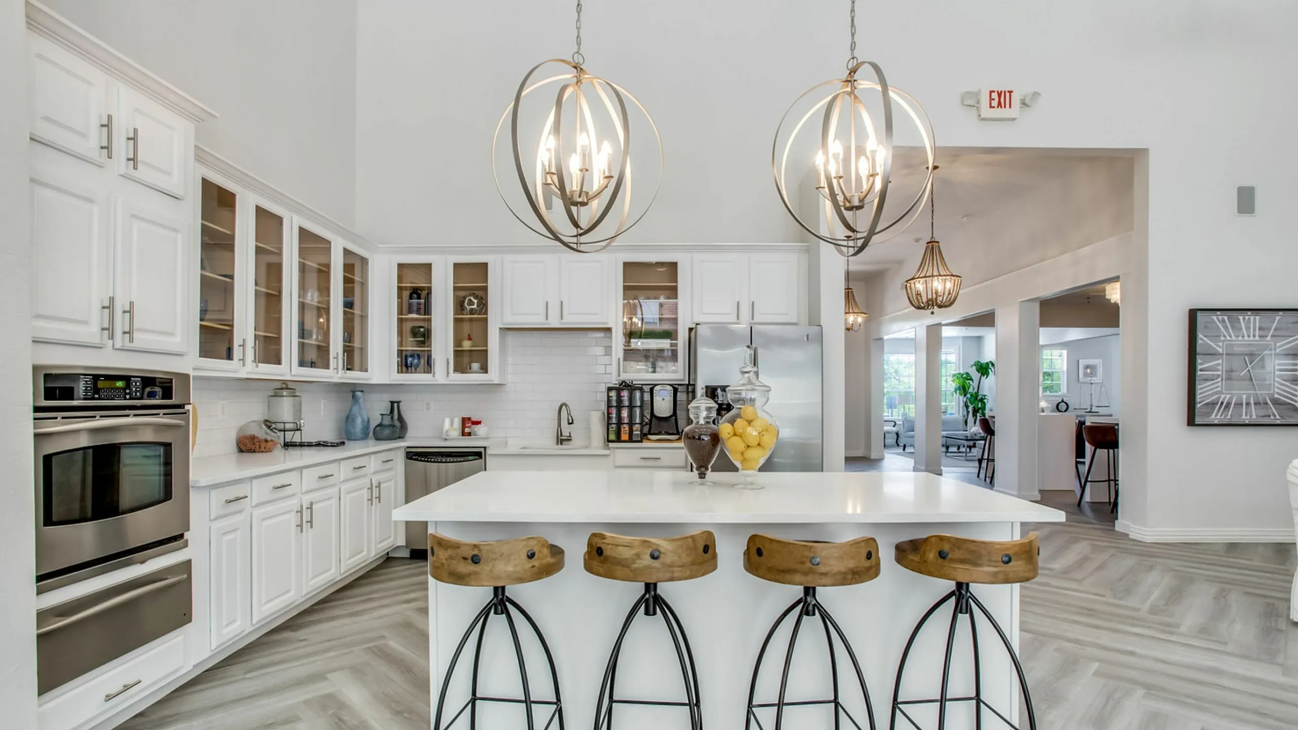 Elegant kitchen with high ceilings featuring a modern chandelier, white cabinetry, and a sleek island with stylish bar stools.