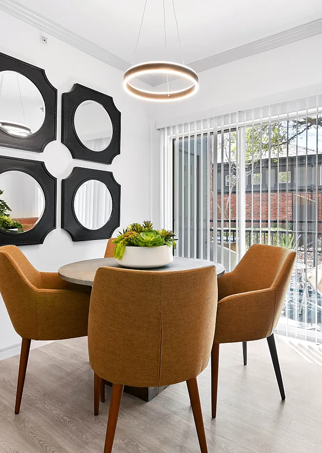 Chic dining area with modern round table, four plush chairs, stylish mirrors, and a soothing natural light ambiance.