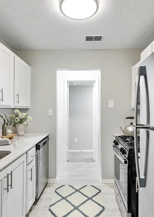 Galley-style apartment kitchen with stainless steel appliances, quartz countertops, white shaker cabinets, subway tile backsplash, and modern finishes.