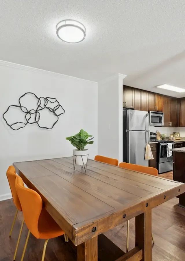Chic dining area with a rustic wooden table and vibrant orange chairs, adjacent to a modern kitchen featuring stainless steel appliances and a sleek breakfast bar.