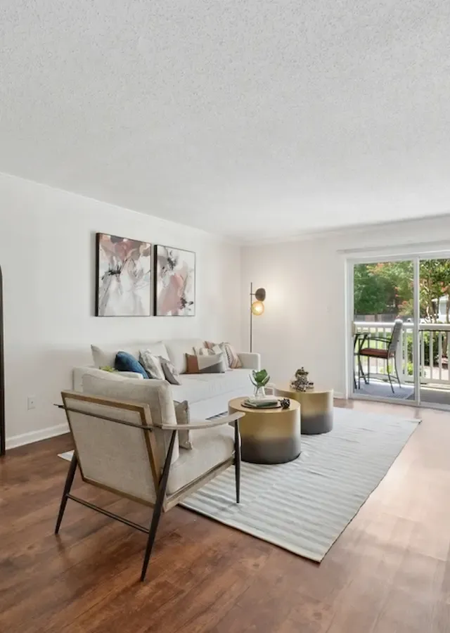 Elegant living room with hardwood floors, stylish decor, and natural light from a large sliding glass door leading to a balcony with garden views.