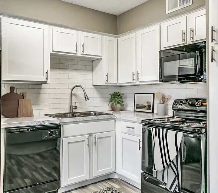 Modern kitchen with white cabinets, marble-style countertops, and black appliances, including an electric stove, microwave, dishwasher, and refrigerator. Features a subway tile backsplash, hardwood-style flooring, and simple countertop deco