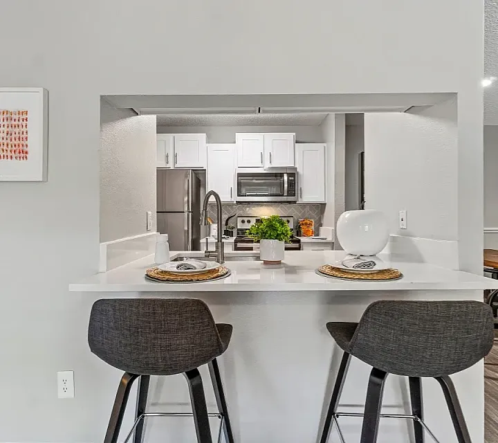 Modern kitchen with a breakfast bar and seating, featuring white cabinetry, stainless steel appliances, and an open pass-through to the dining area.