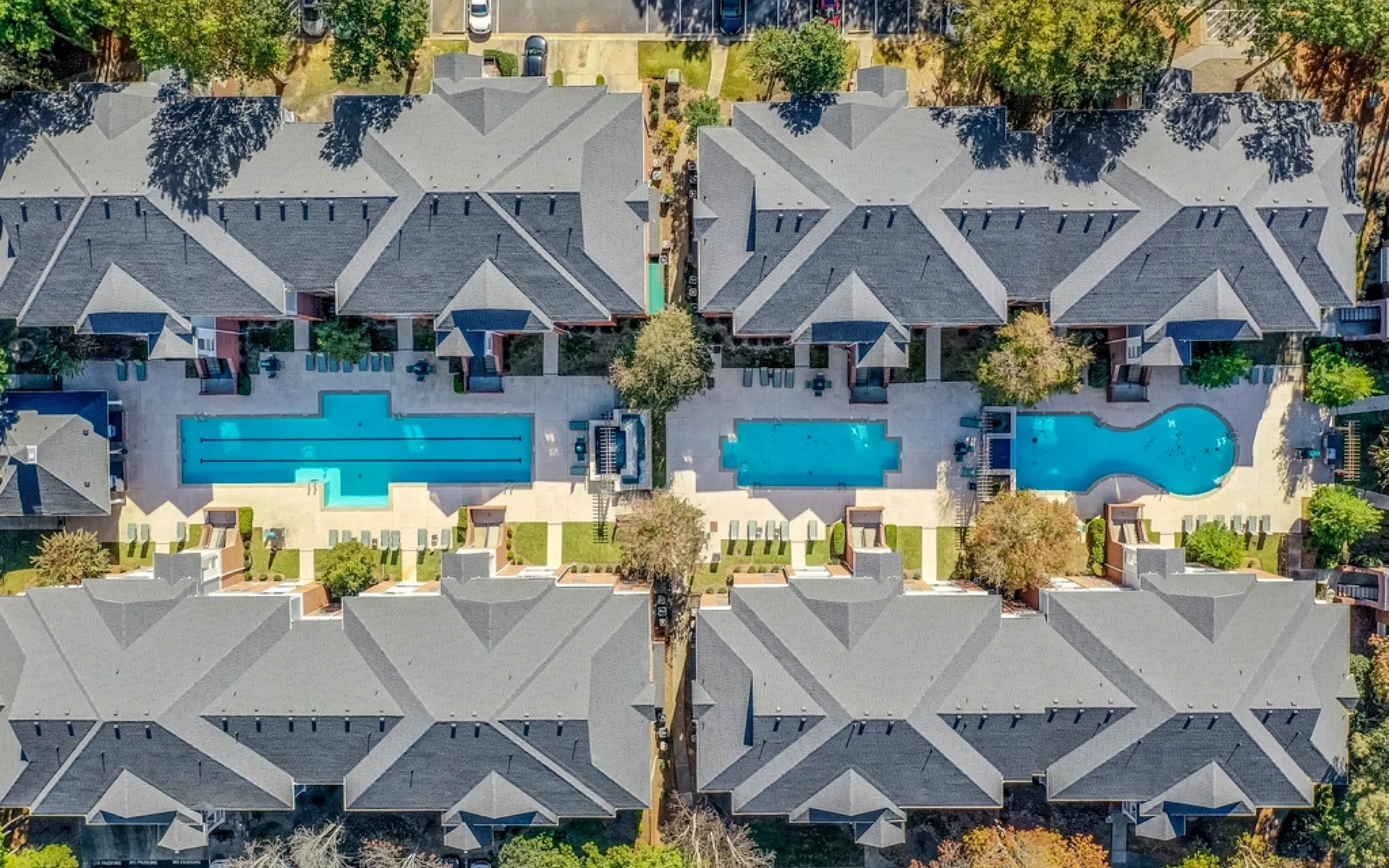 Aerial view of a modern apartment community featuring multiple resort-style swimming pools, spacious sundecks, landscaped courtyards, and contemporary residential buildings surrounded by greenery.