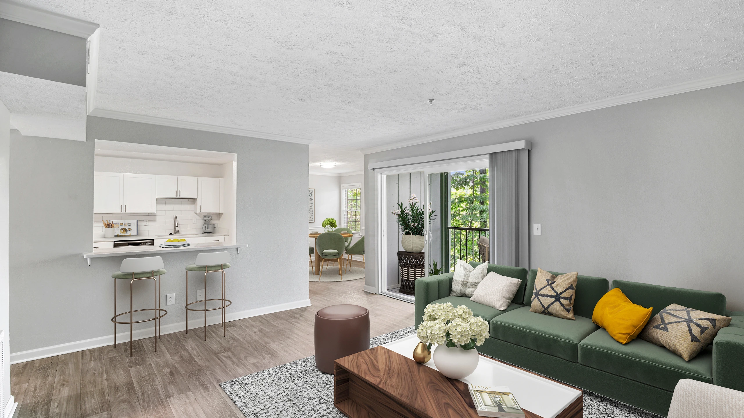 Bright open-concept living room and kitchen with wood-style flooring, a breakfast bar with seating, and modern white cabinetry. The space features a green sofa with accent pillows, a cozy dining area, and sliding glass doors leading to a pr