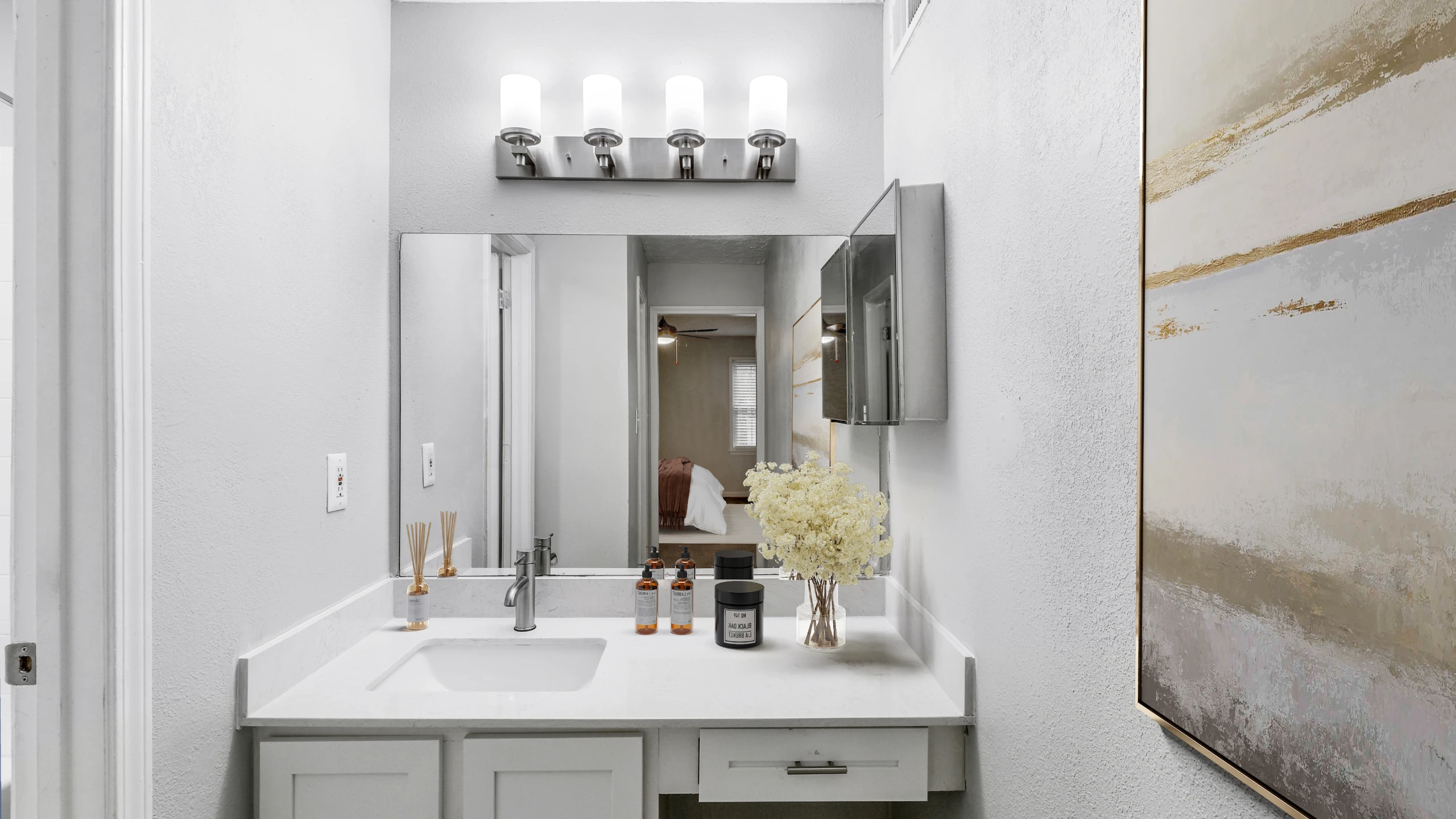 Modern bathroom vanity with a sleek white countertop, undermount sink, brushed nickel fixtures, and contemporary lighting. The space features a large mirror, minimalist d&eacute;cor accents, soft neutral tones, and abstract wall art for a c