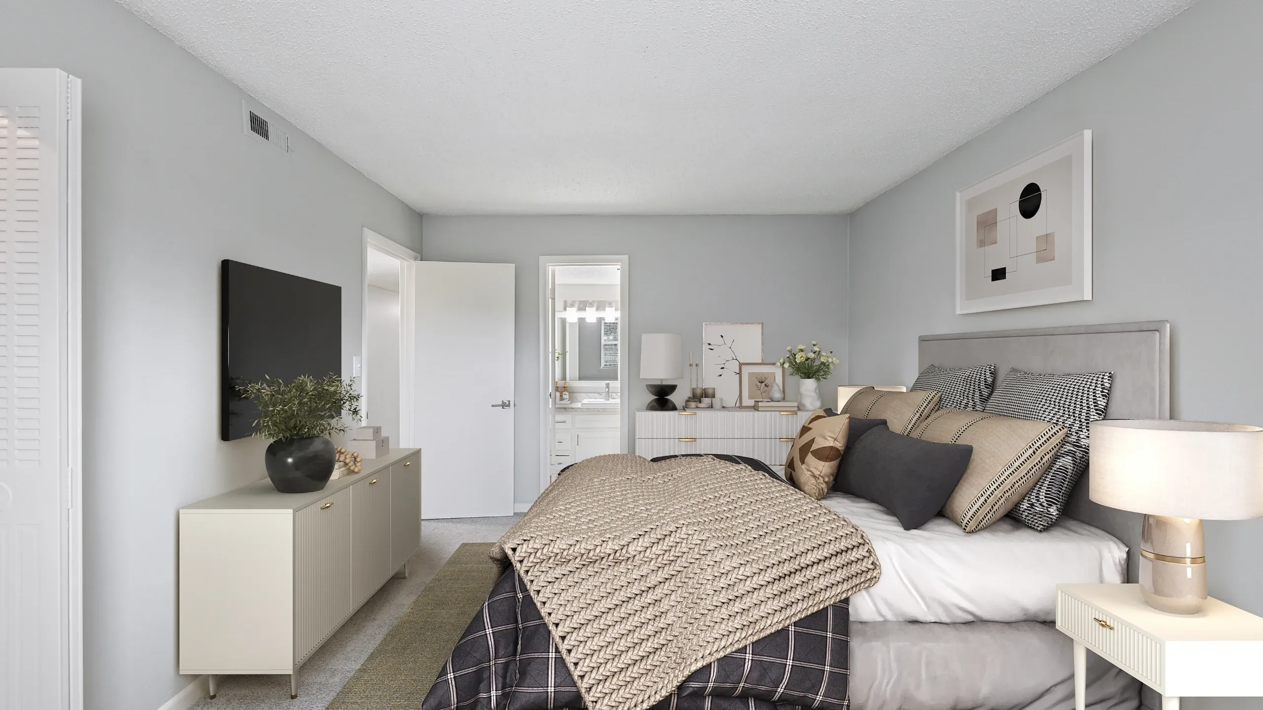 Contemporary bedroom with soft gray walls, a large upholstered bed, layered neutral bedding, and modern decor accents. The room features matching nightstands, a dresser with a mounted TV, framed artwork, and warm lighting, creating a clean