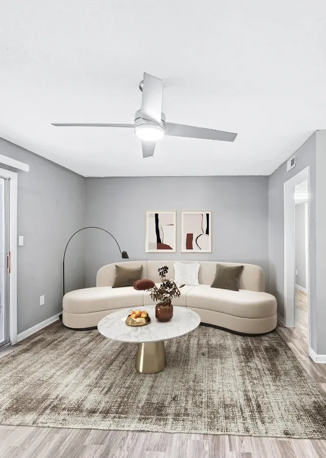 Contemporary living room with a curved cream-colored sofa, textured area rug, and round marble coffee table with gold accents. Soft gray walls, abstract artwork, and minimalist decor create a modern and inviting atmosphere, while a ceiling