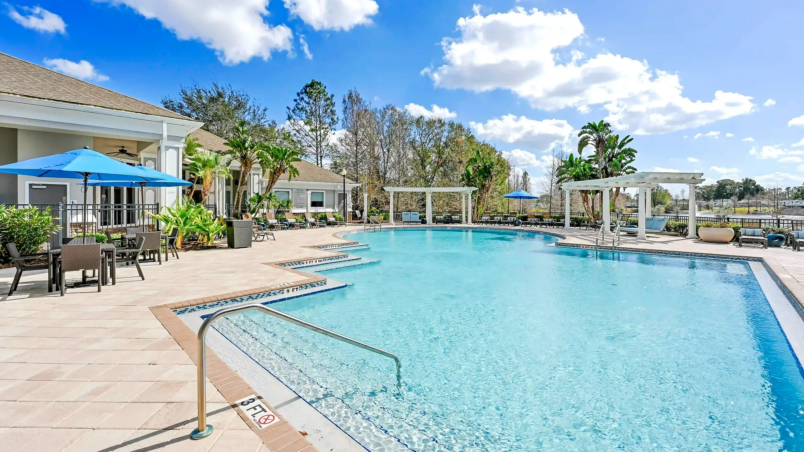 Luxurious poolside view of a serene residential complex with stylish patio seating and lush landscaping, perfect for relaxation and entertainment.