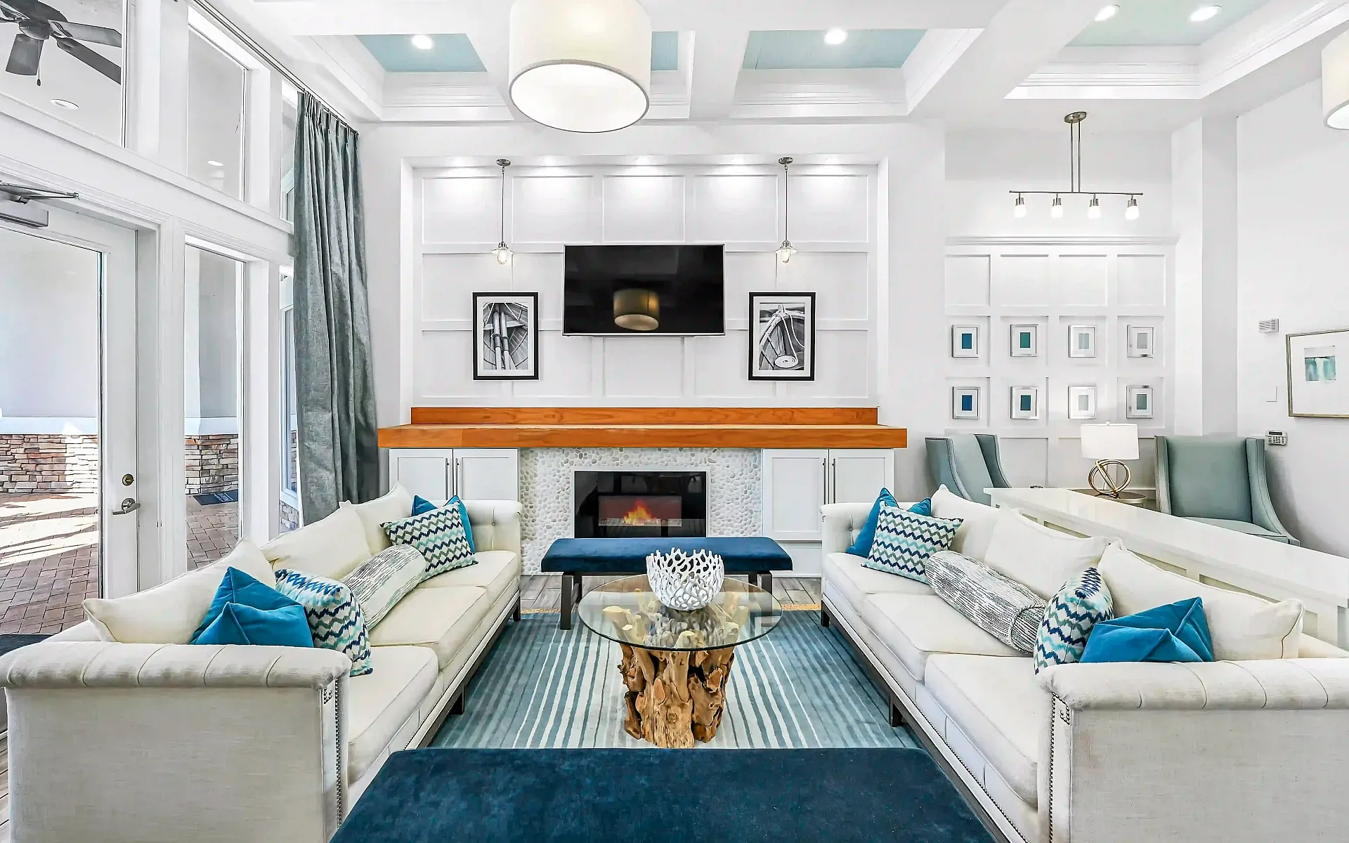 Luxurious clubhouse with chic white sofas, vibrant blue accents, modern fireplace, and elegant decor in a bright, open-concept space.