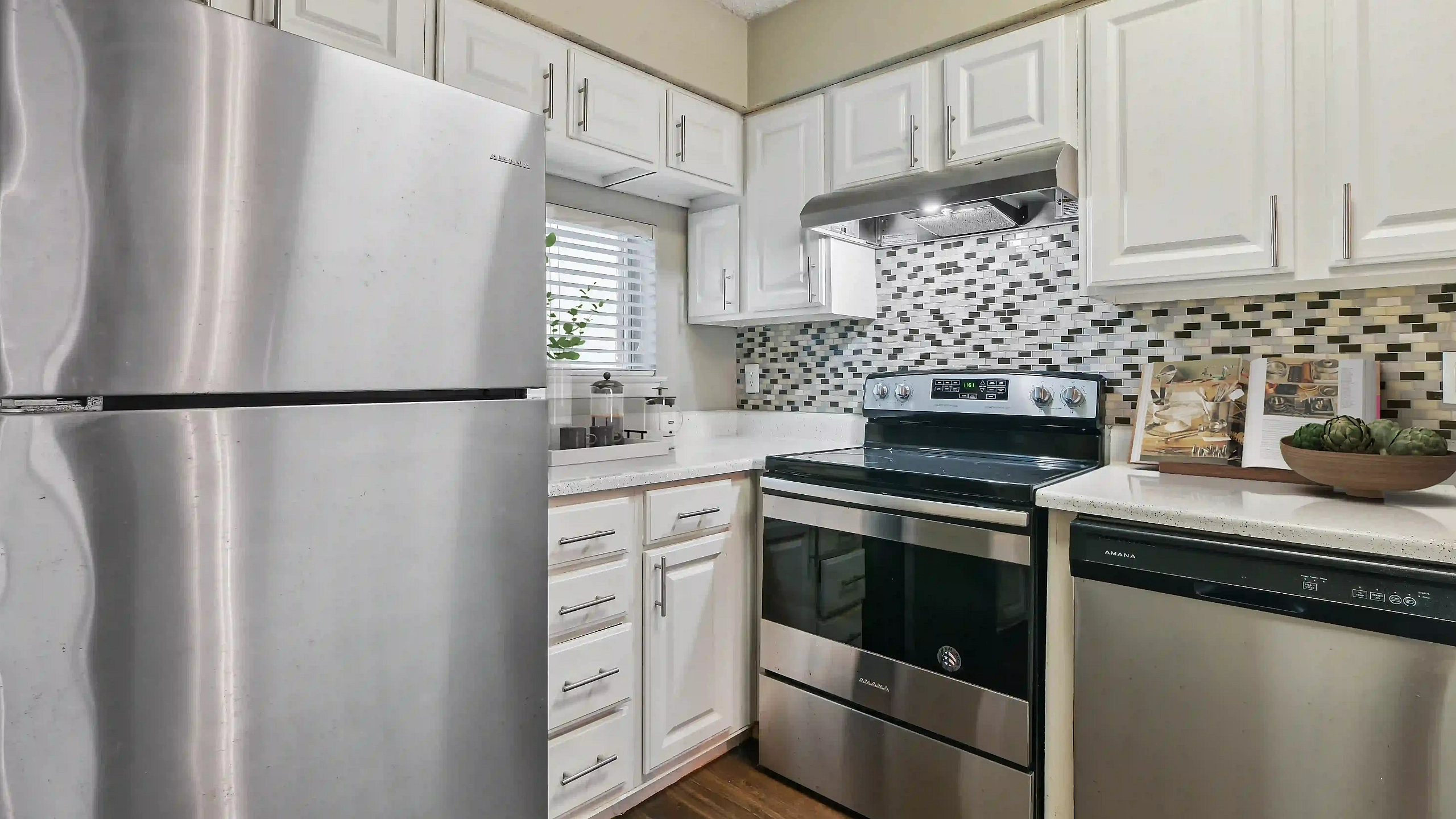 Modern kitchen with stainless steel appliances, sleek white cabinetry, and mosaic tile backsplash.
