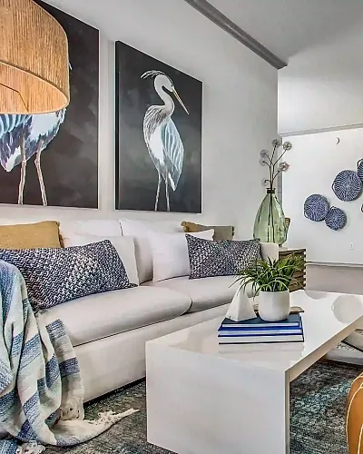 Modern living area with elegant decor, featuring a cozy white sofa, stylish bird artwork, and a sleek open kitchen.