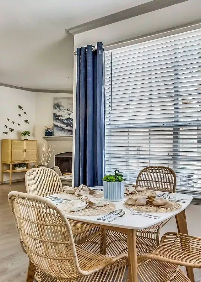 Elegant dining area with wicker chairs and a sunlit window, adjacent to a modern open-plan kitchen with stylish decor.