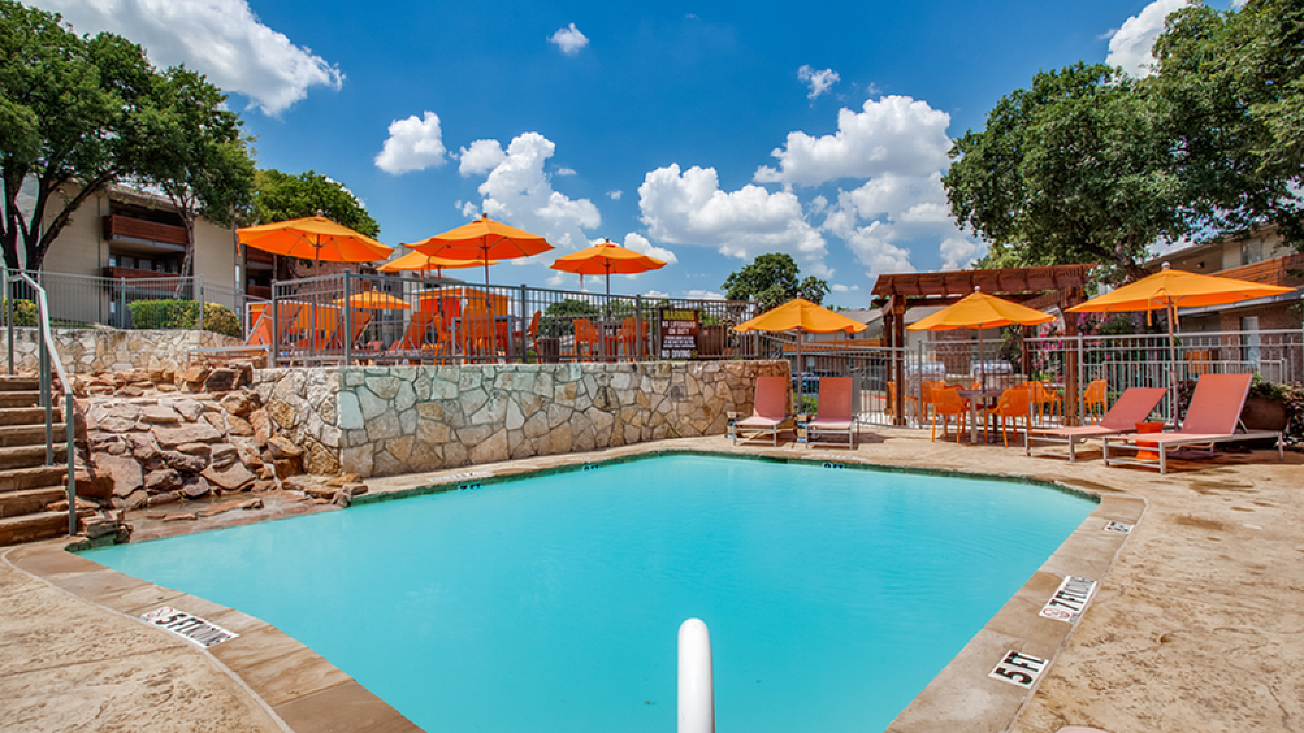 Inviting swimming pool area with vibrant orange umbrellas and stylish lounge chairs under a bright blue sky.