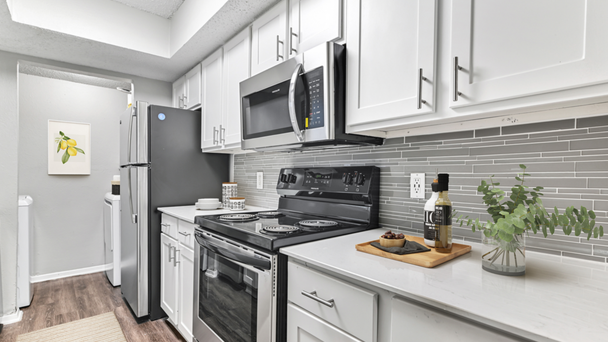 Contemporary kitchen with sleek stainless steel appliances, elegant white cabinetry, and stylish gray backsplash, offering a chic cooking experience.