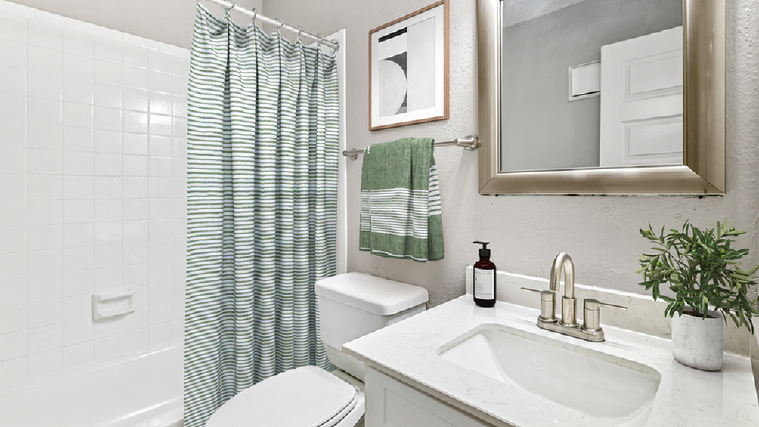 Chic modern bathroom with elegant vanity, stylish mirror, and a relaxing bathtub with striped shower curtain.