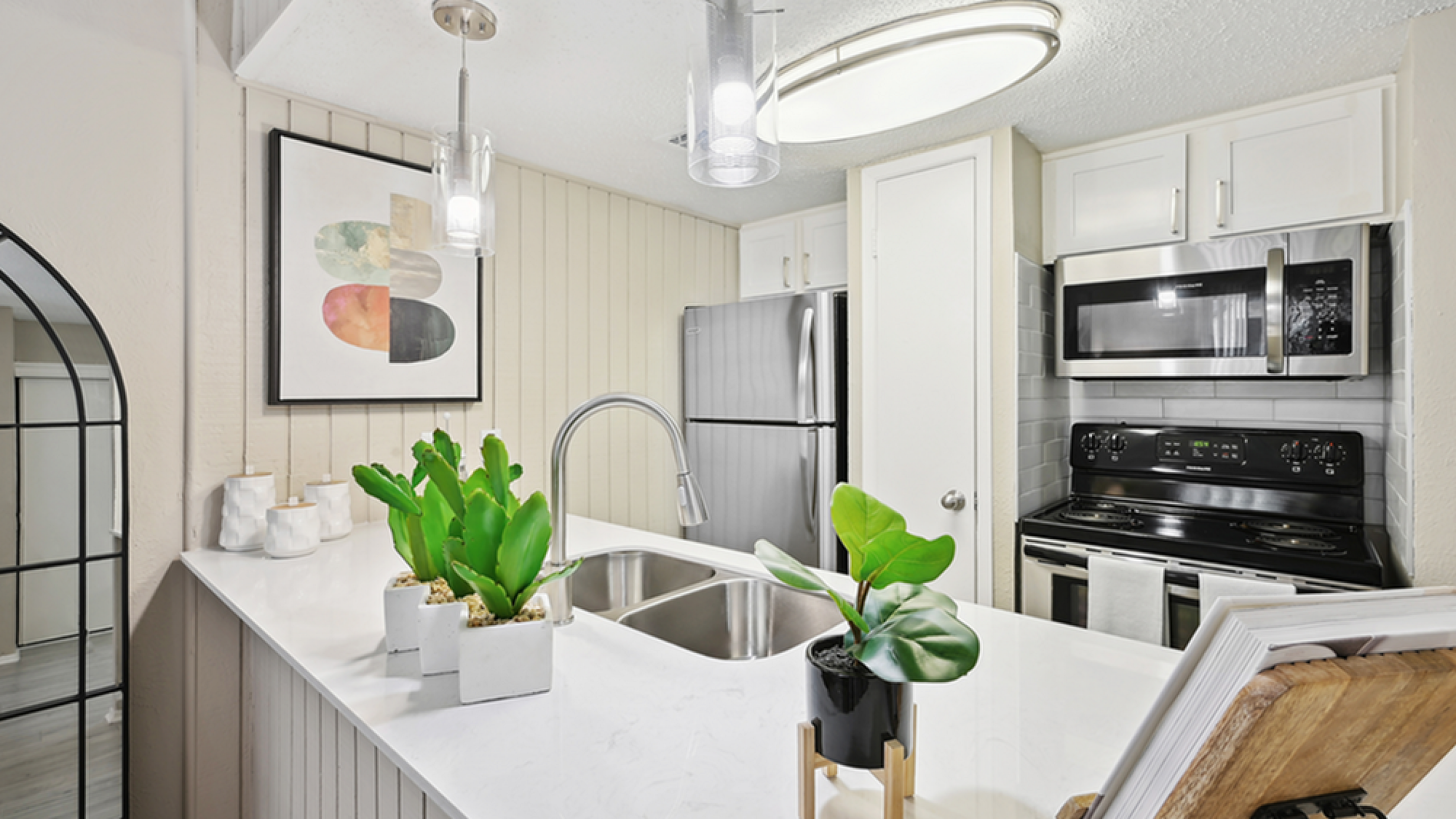 Modern kitchen featuring stainless steel appliances, elegant pendant lighting, and a chic countertop with stylish plants.