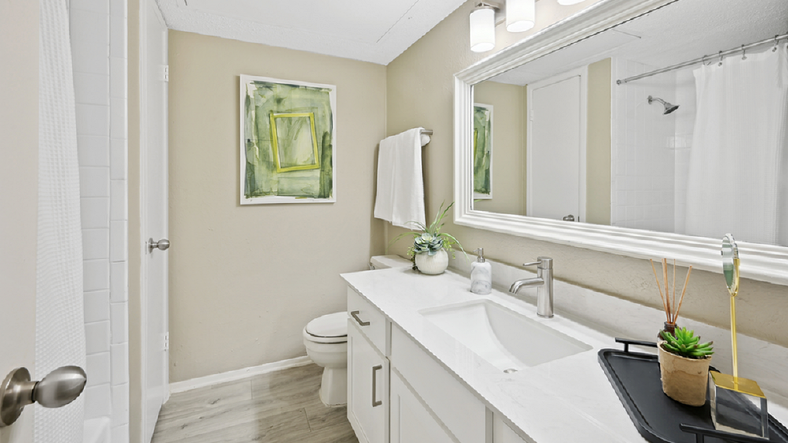 Elegant bathroom with modern fixtures, large mirror, and contemporary decor, featuring stylish lighting and fresh greenery accents.