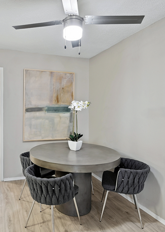 Modern dining area with a sleek round table and stylish gray chairs, enhanced by a chic ceiling fan and contemporary artwork.