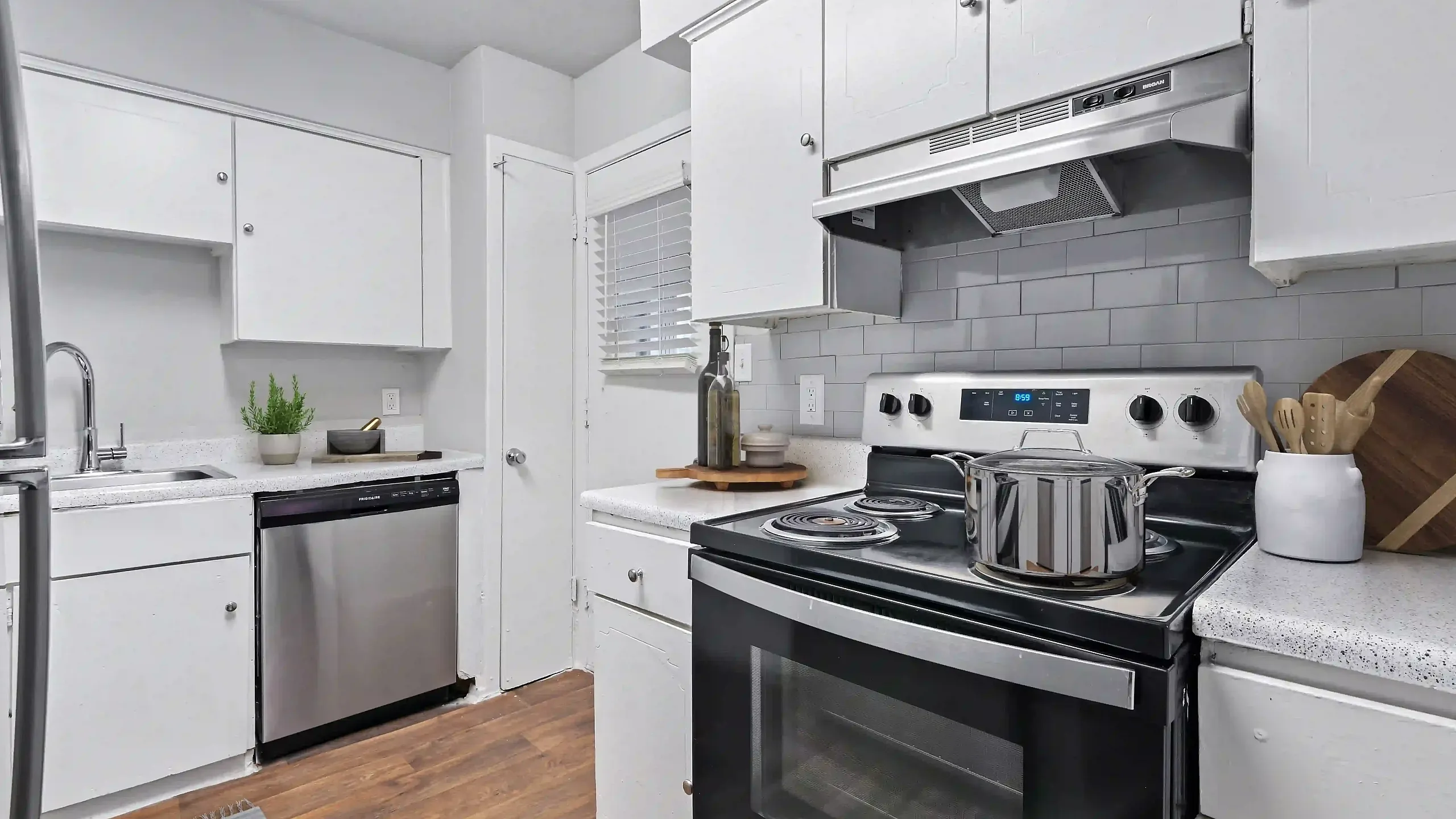 Bright and modern kitchen featuring sleek stainless steel appliances, elegant white cabinetry, and rich wooden flooring.