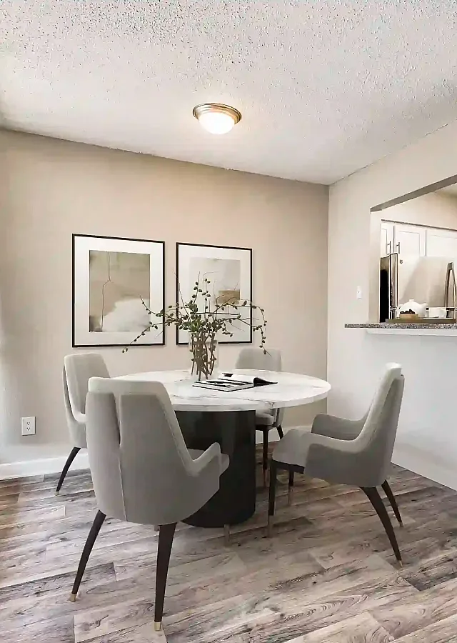 Bright and inviting dining area with a chic round table, stylish gray chairs, and modern decor seamlessly opening into a sleek kitchen space.