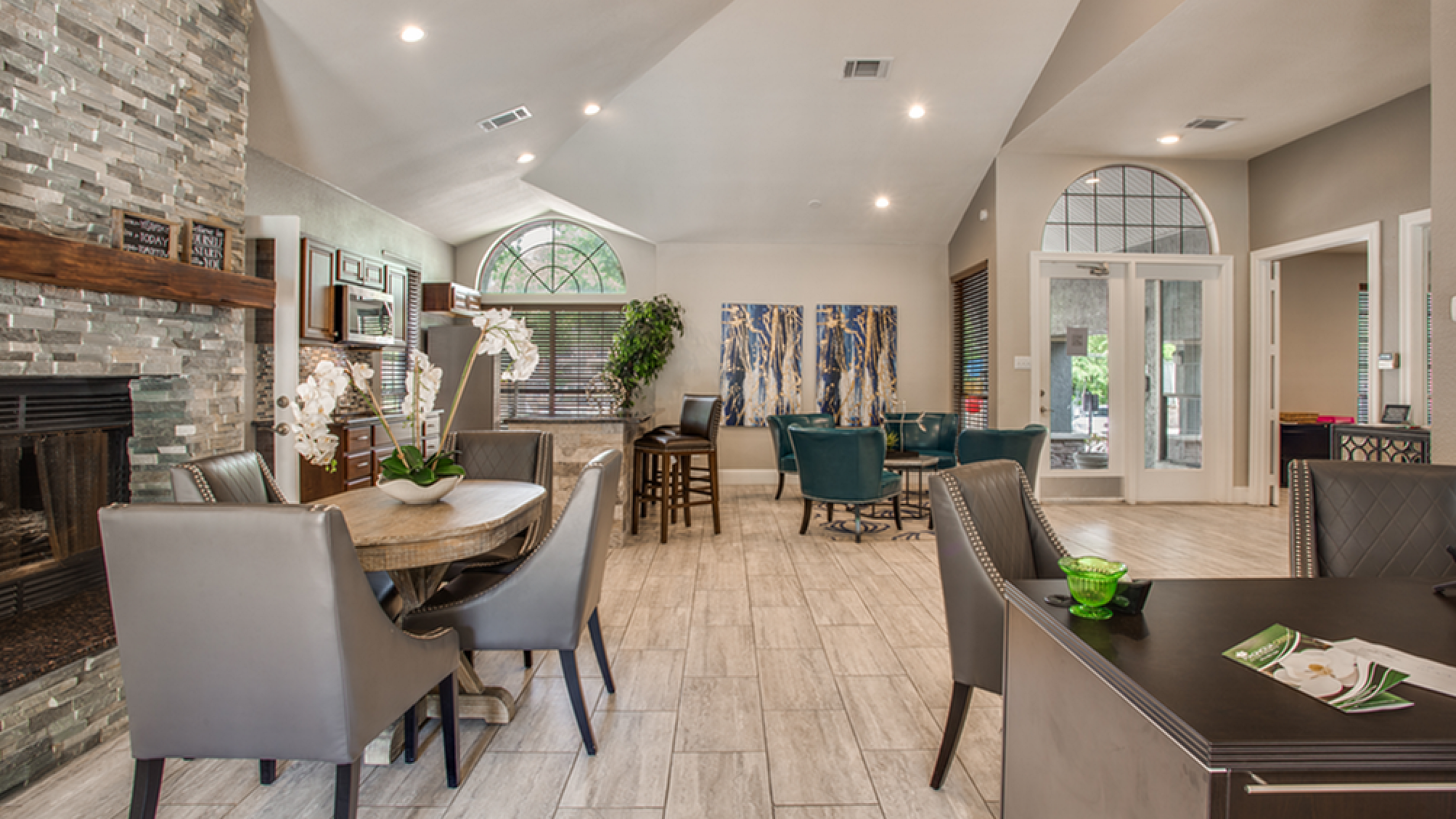 Modern and inviting communal area featuring a cozy stone fireplace, elegant dining setup, and vibrant teal seating, ideal for gatherings.