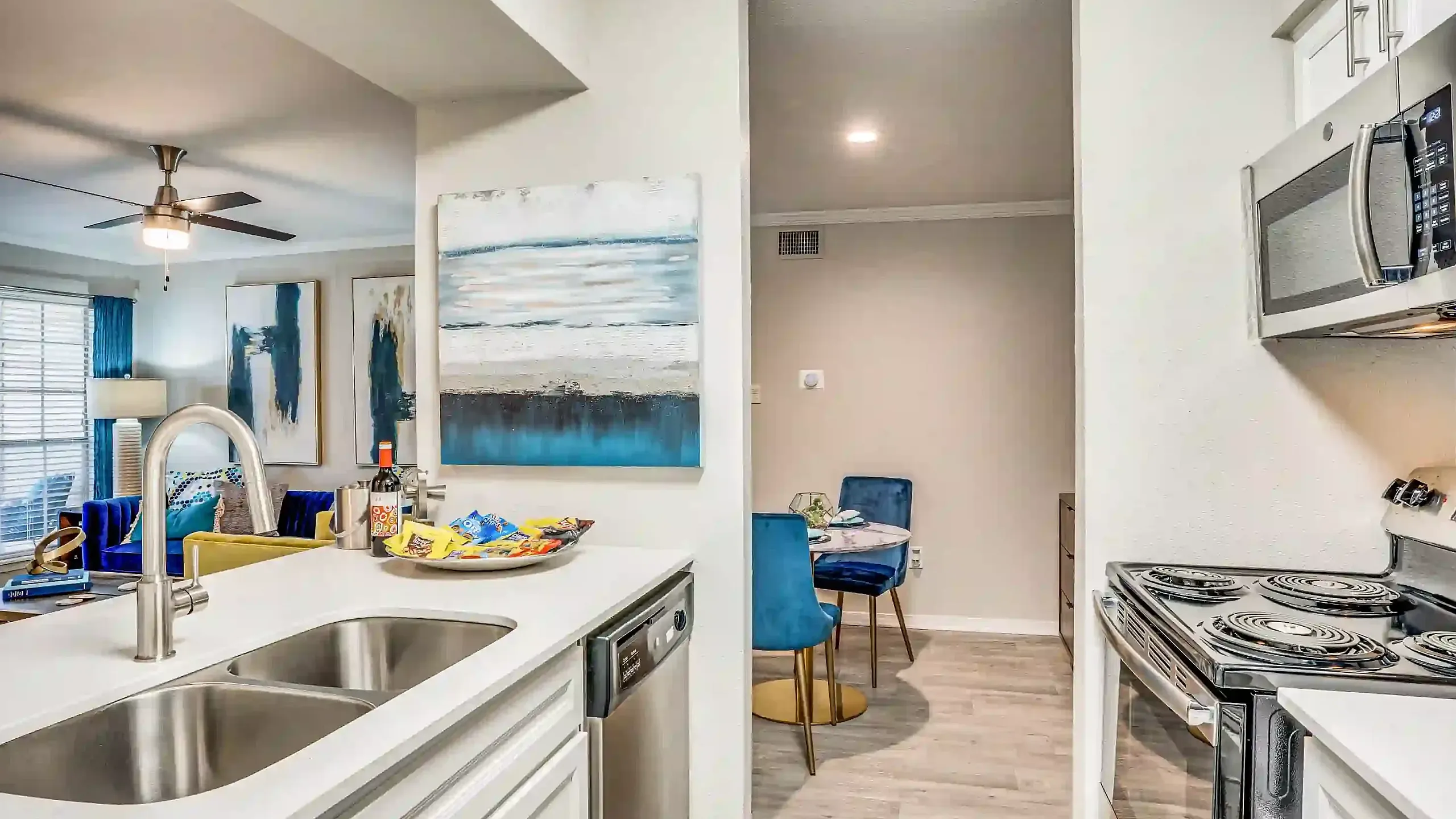 Modern open-concept apartment kitchen with stainless steel appliances, stylish dining area, and vibrant living room with artistic decor.