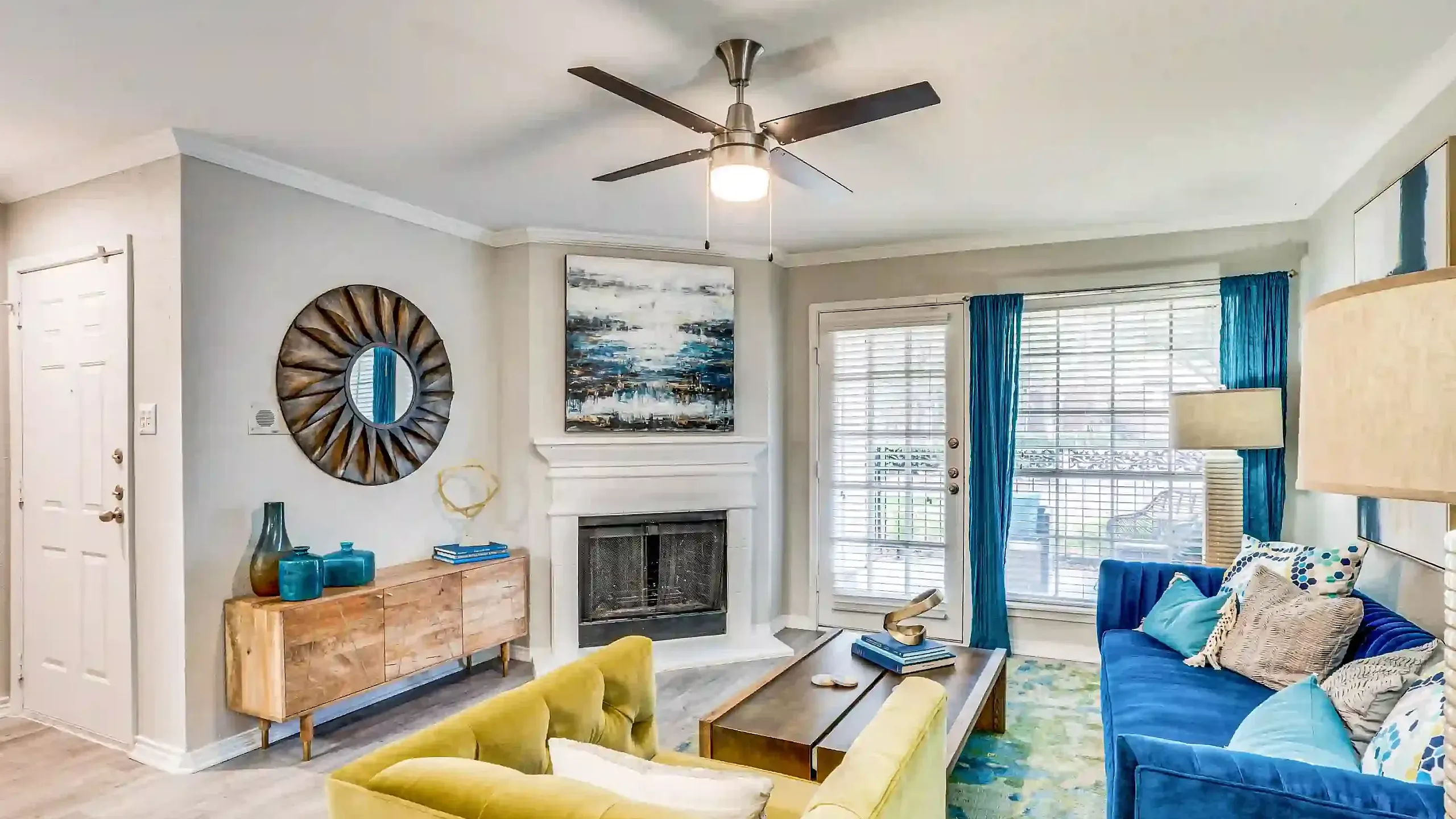 Chic living room with vibrant blue and yellow seating, modern decor, and cozy fireplace, enhanced by natural light.